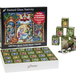 May include: A 1000 piece jigsaw puzzle advent calendar with a stained glass nativity scene. The box is open and shows the 24 individual puzzle pieces, each with a number from 1 to 24. The back of the box shows the completed puzzle and the text "24 Day Countdown to Christmas!"