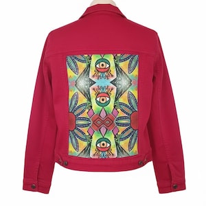 Puede incluir: Chaqueta vaquera roja con un diseño geométrico colorido en la espalda. La obra de arte presenta formas de ojo y elementos florales en tonos de amarillo, verde, azul y rosa. La chaqueta tiene un diseño clásico con botones.