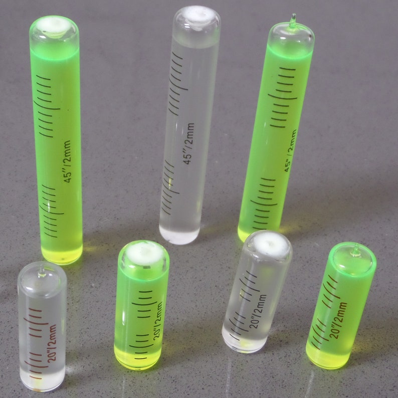 May include: Seven glass vials containing green liquid with markings in inches and millimetres. The vials are labelled with measurements in inches and millimetres, such as 20"/2mm and 45"/2mm.