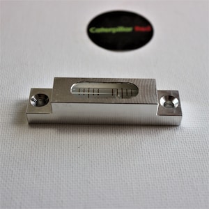 May include: A silver metal level with a clear glass bubble and a graduated scale. The level has two holes on either side.