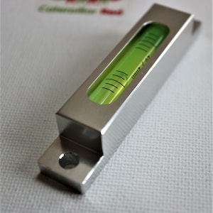 May include: A silver metal level with a green bubble level. The level has a hole on one side and a rectangular shape.