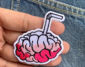 May include: Embroidered patch showing a brain design with a straw, like a brain freeze. The brain is in pink and red shades, with a white outline and a black and white straw. The patch is set against a denim background.