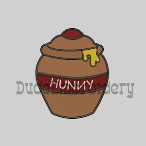 Può includere: Un vaso di miele in ceramica marrone con un coperchio rosso e un goccio di miele giallo. Il vaso ha la scritta "HUNNY" in bianco.