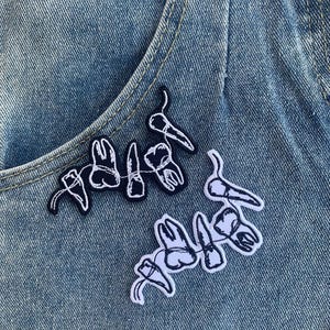 Może przedstawiać: Dwa haftowane naszywki z zębami na niebieskim tle z dżinsu. Naszywki są czarne i białe i przedstawiają ciąg zębów.