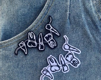 May include: Two embroidered patches of teeth on a blue denim background. The patches are black and white and feature a string of teeth.