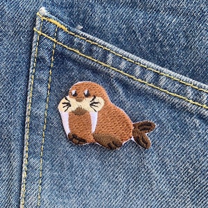 May include: A brown embroidered walrus patch with white tusks, sitting on a blue denim pocket.