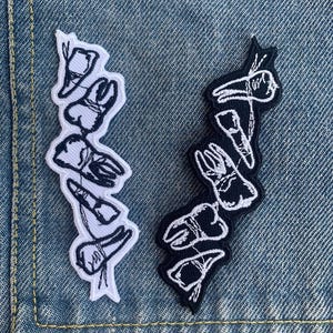 May include: Two embroidered patches, one white and one black, each featuring a stylized dental illustration. The white patch has a black outline, while the black patch has a white outline. Both patches are on a denim background.