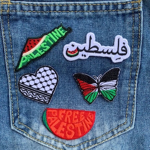 May include: Close-up of a denim pocket adorned with embroidered patches. Patches include a watermelon slice with "Palestine" text, a heart with a black and white pattern, and a butterfly with Palestinian flag colors.
