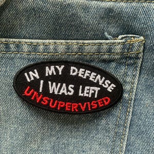 May include: A black and red embroidered patch with the text "In my defense I was left unsupervised".