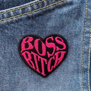 Pode incluir: Patch em forma de coração rosa e preto com o texto "Boss Bitch" bordado.