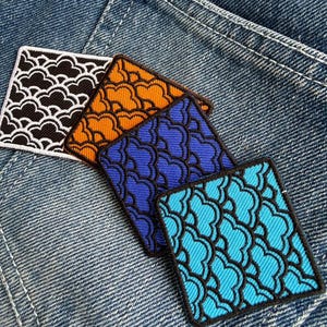 May include: Four square embroidered patches with a repeating cloud-like pattern in black, orange, blue, and turquoise. Each patch has a black border and is displayed on a denim background.