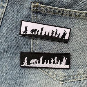 May include: Two embroidered patches on a blue denim background. The patches are rectangular and feature a white silhouette of a group of people walking with a horse. The top patch is black with white stitching, and the bottom patch is white with black stitching.