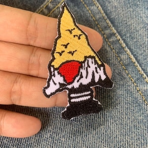 May include: Embroidered patch with a mountain design. It features a yellow peak, white snowy areas, and a red heart. The patch has a black base and is designed for clothing or accessories.