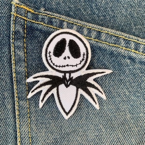 Könnte beinhalten: Weißer gestickter Aufnäher von Jack Skellington, dem Kürbis-König aus Nightmare Before Christmas, auf blauem Jeansstoff.