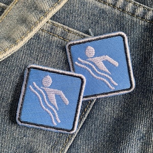 May include: Two blue and white embroidered patches with a swimmer icon on a denim background.