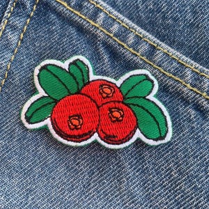 May include: A red and green embroidered patch of three cranberries with white outlines on a blue denim background.