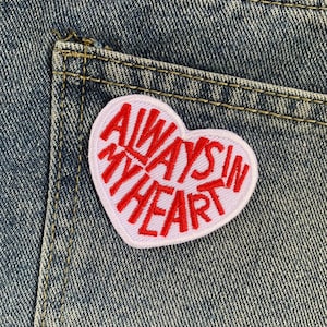 以下が含まれることがあります： 「Always in my heart」と赤い刺繍で書かれたピンクのハート型のワッペンです。