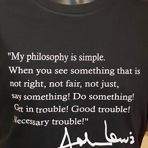 May include: Black t-shirt featuring a quote by John Lewis in white text: "My philosophy is simple...say something! Do something! Get in trouble! Good trouble! Necessary trouble!" Includes his signature.