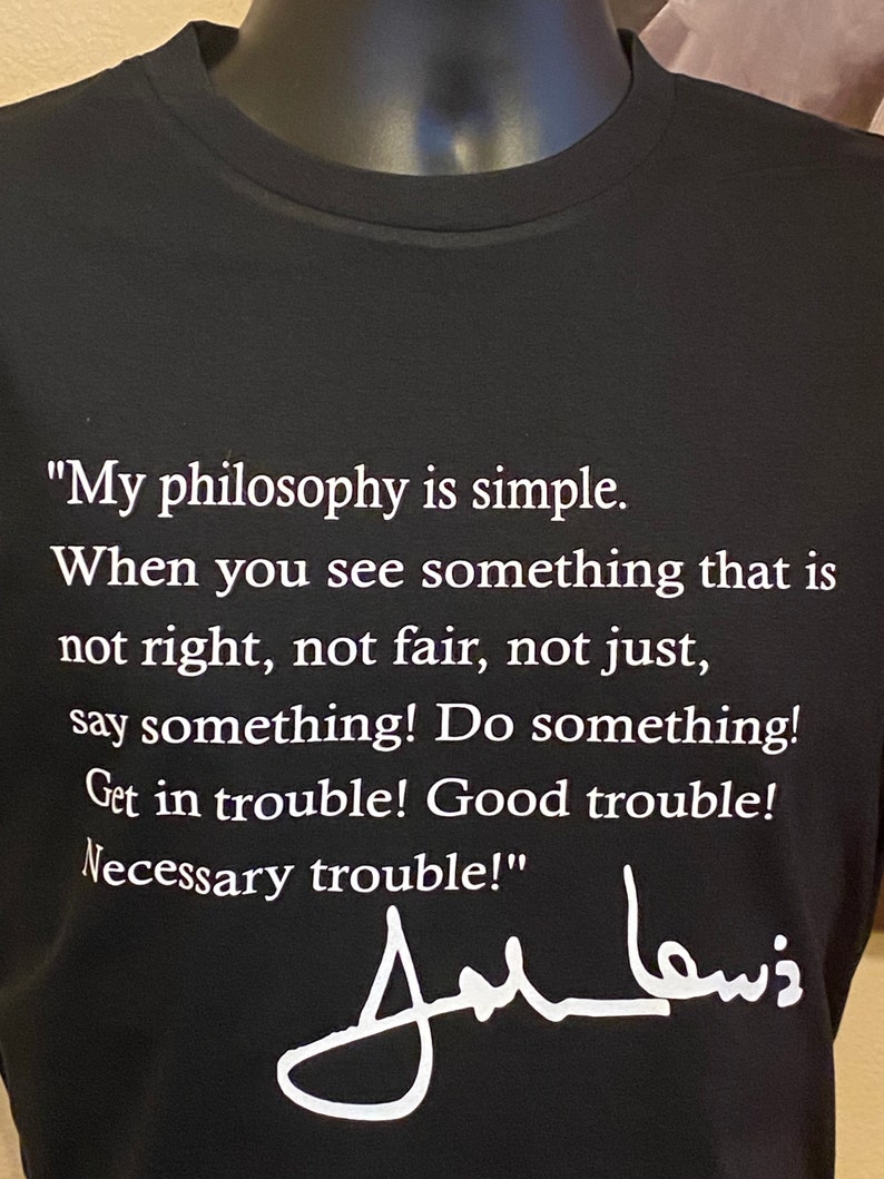 May include: Black t-shirt featuring a quote by John Lewis in white text: "My philosophy is simple...say something! Do something! Get in trouble! Good trouble! Necessary trouble!" Includes his signature.