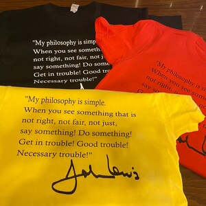 May include: Four t-shirts in black, red, and yellow are displayed. Each shirt features the quote "My philosophy is simple...say something!" and a signature. The shirts are made of a soft material.