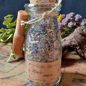 May include: A glass jar with a cork lid and a wooden handle filled with a mixture of dried herbs and bath salts. The jar has a brown paper label that reads "Ritual Bath - Moon Magic".