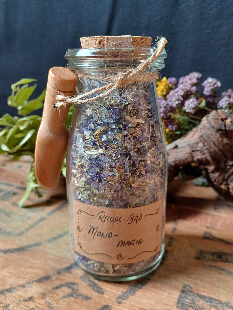 May include: A glass jar with a cork lid and a wooden handle filled with a mixture of dried herbs and bath salts. The jar has a brown paper label that reads "Ritual Bath - Moon Magic".