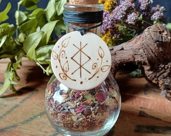 May include: A clear glass bottle with a cork stopper and a wooden charm with a symbol and leaves. The bottle is filled with dried herbs and flowers.
