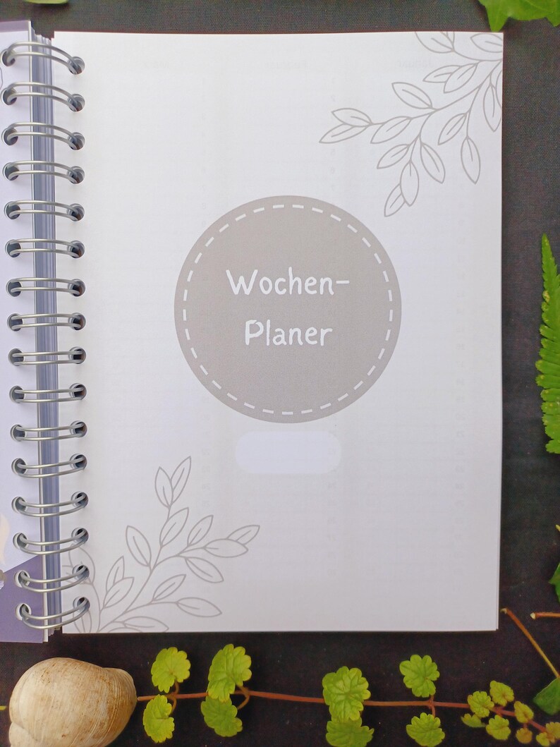 May include: A gray and white weekly planner with a circle on the front that says "Wochen-Planer" in a gray font.