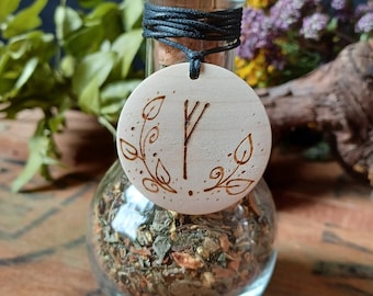 May include: A small glass bottle with a cork stopper and a wooden pendant. The pendant is round and has a carved symbol and leaves. The bottle is filled with dried herbs.