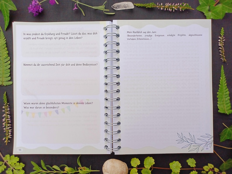 May include: A white spiral bound journal with a green cover. The cover has a wavy edge and features text in German. The text reads: "In was findest du Erp&uuml;llung und Freude? L&auml;sst du das, was dich erf&uuml;llt und Freude bringt, oft genug in dein Leben?"  "Nemst du dir ausreichend Zeit f&uuml;r dich und deine Bed&uuml;rfnisse?"  "Wann waren deine gl&uuml;cklichsten Momente in deinem Leben? Was war daran so besonders?"  "Mein R&uuml;ckblick auf den Juni:  Beziehungen, Freude, Errungenschaften, wichtige Projekte, abgeschlossene Vorhaben, Erkenntnisse..."