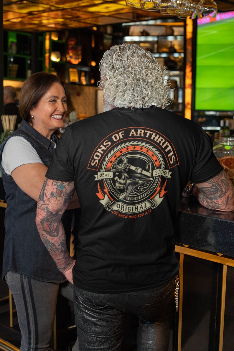 May include: Black t-shirt with a graphic of a skull wearing a helmet and the text "Sons of Arthritis Est. 2009 Original You Know Who You Are".