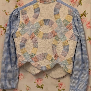 Peut inclure: Une veste courte en vichy bleu et blanc avec un panneau arri&egrave;re matelass&eacute; pr&eacute;sentant un motif patchwork de couleurs pastel et de motifs floraux.