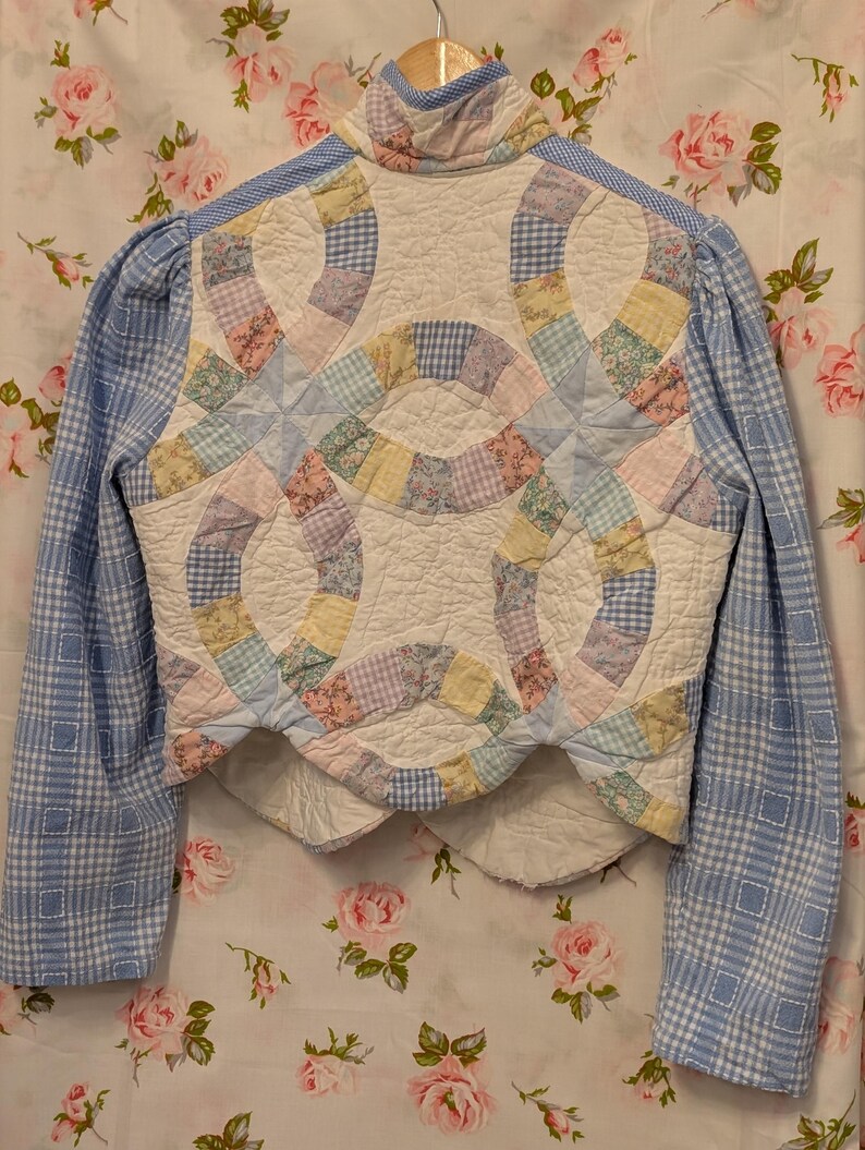 Peut inclure: Une veste courte en vichy bleu et blanc avec un panneau arri&egrave;re matelass&eacute; pr&eacute;sentant un motif patchwork de couleurs pastel et de motifs floraux.