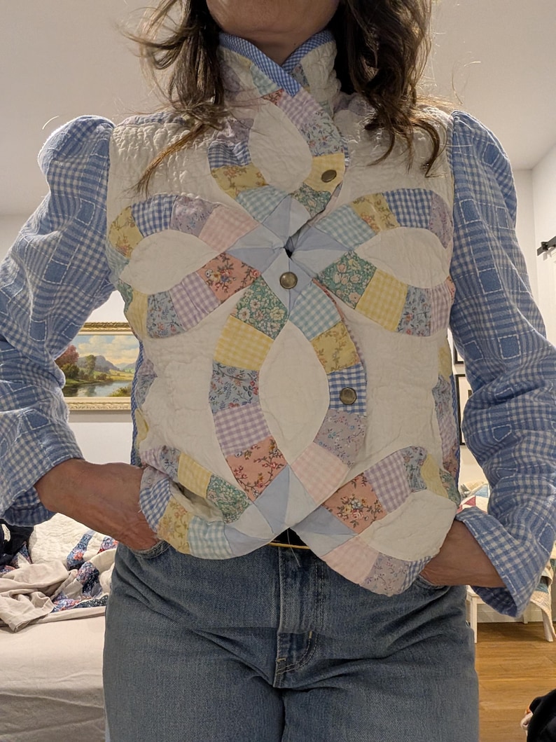 Peut inclure: Un gilet matelass&eacute; blanc avec un motif patchwork color&eacute;. Le gilet a un col montant et une fermeture &agrave; boutons. Le motif patchwork pr&eacute;sente une vari&eacute;t&eacute; de motifs floraux et g&eacute;om&eacute;triques dans des tons de rose, bleu, jaune et vert.