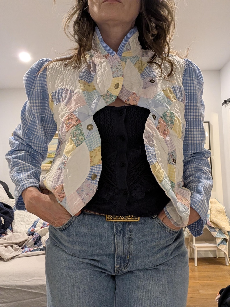 Peut inclure: Une veste en patchwork bleu et blanc avec un col montant et des manches bouffantes. La veste est en tissu matelass&eacute; et se ferme par des boutons. La veste est port&eacute;e sur un haut en maille noir et un jean bleu.