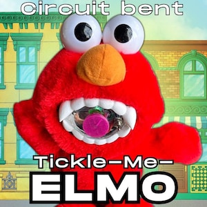 May include: A red plush toy with large white googly eyes and an orange nose. The mouth is open, revealing white teeth and a clear plastic component containing a pink circular dial. The text "circuit bent" and "Tickle-Me-ELMO" appear in white.