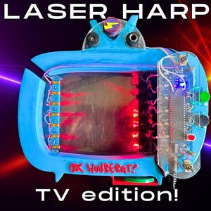 May include: A blue laser harp TV edition device featuring the text LASER HARP and TV EDITION! with OK HOUSECAT! printed on the front. The electronic instrument includes a circuit board, red laser beams, toggle switches, and a central display area.