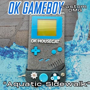 May include: Custom DMG Gameboy with a blue and yellow screen, blue buttons, and the text "OK HOUSECAT" and "Aquatic Sidewalk". The Gameboy is gray with a textured finish.