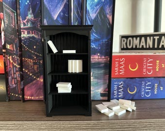 May include: A black bookshelf with three shelves, each filled with white books. The bookshelf is against a wall with a bookshelf on either side. The bookshelves are decorated with images of a city and a snowy landscape. The text "ROMANTAS" is visible on a book on the top shelf.