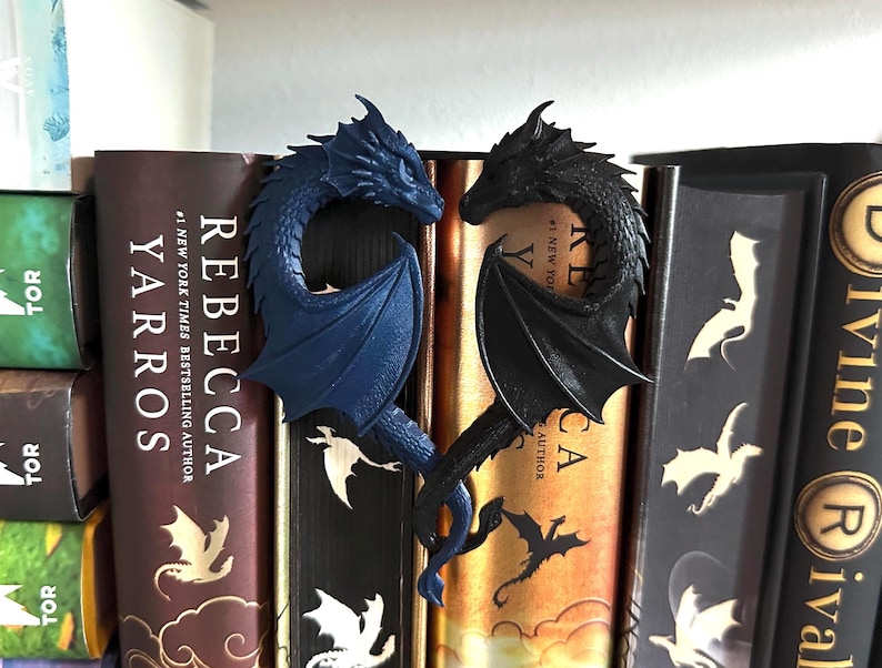 May include: Two dragon bookends, one blue and one black, with wings outstretched. The bookends are placed on a bookshelf with several books visible.