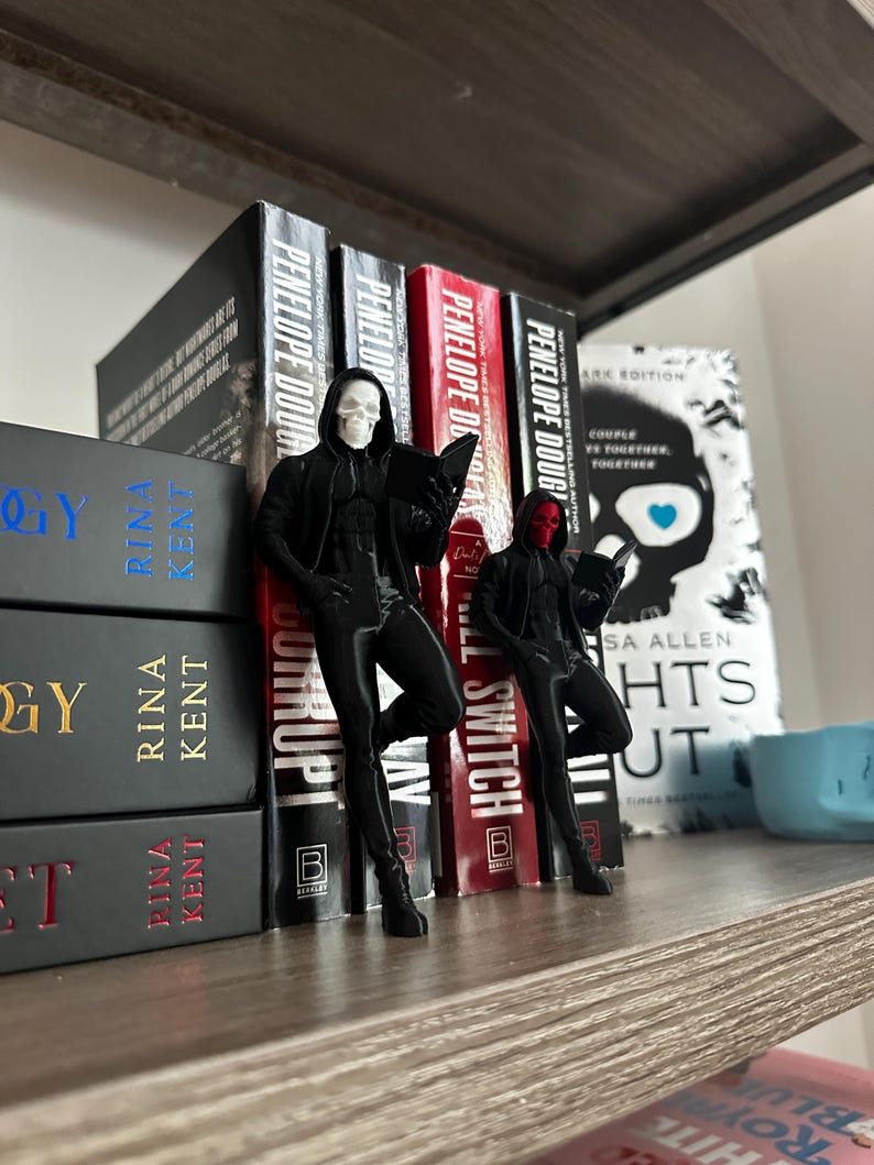 Puede incluir: Dos figuras negras de una persona con capucha, una con una m&aacute;scara de calavera blanca y la otra con una m&aacute;scara roja, se colocan frente a una fila de libros. Los libros tienen t&iacute;tulos como "Penelope Douglas" y "Lights Out."