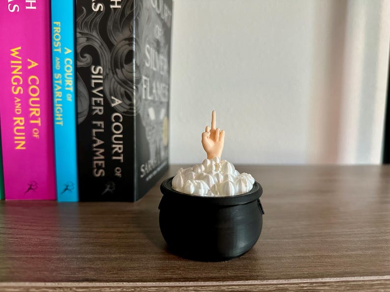 Op de afbeelding: Een zwarte ketel met een witte, schuimige substantie erin. Een hand met een opgestoken middelvinger steekt uit het schuim.