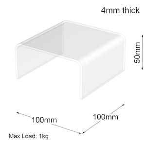 May include: A clear acrylic display stand, measuring 10cm x 10cm, 5cm high, and 4mm thick. The stand has rounded corners and a maximum load capacity of 1kg. The text "Max Load: 1kg" is visible.