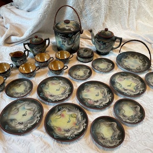 May include: A black and white dragon tea set with a teapot, creamer, sugar bowl, and 12 cups and saucers. The set is decorated with a dragon design and has a gold trim.