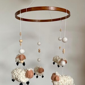 May include: A white wooden baby mobile with five white felt sheep and wooden beads hanging from a brown wooden ring.