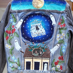 Puede incluir: Una chaqueta de mezclilla gris con un diseño pintado a mano en la espalda que muestra un cielo nocturno con luna llena, una cama con un perro negro, cuatro fantasmas blancos y una casa con una guitarra y un osito, rodeado de rosas rojas y margaritas.