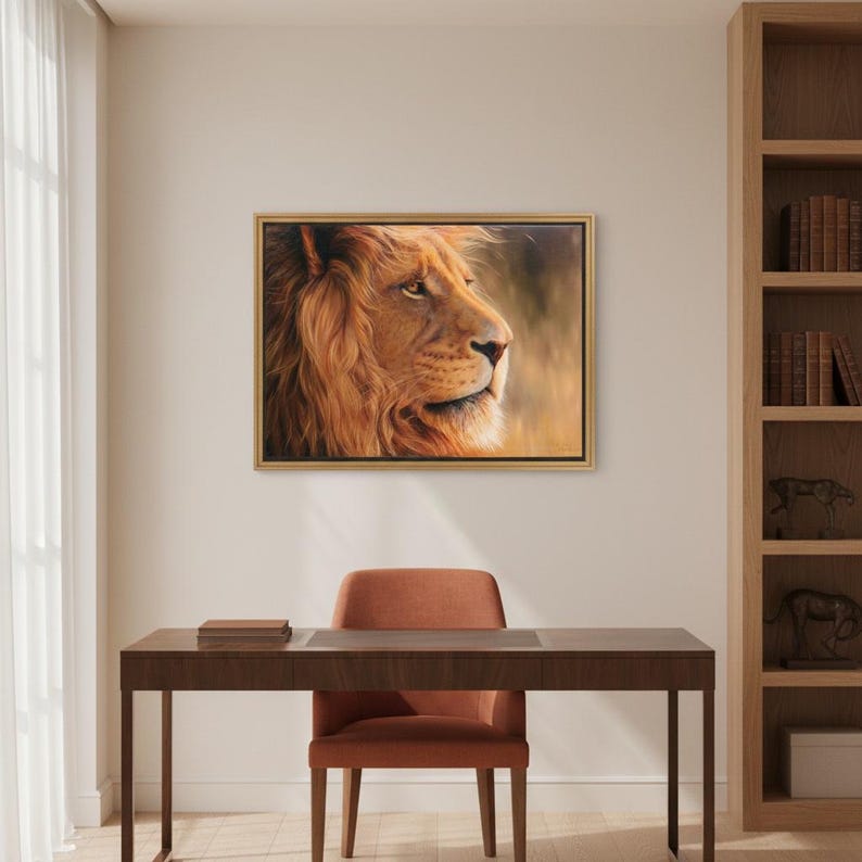 May include: A framed artwork depicts a detailed portrait of a lion's head in profile. The lion's fur is a warm, golden-brown color, with a flowing mane. The artwork is set in a gold frame, and hangs above a desk and chair.