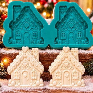 May include: A teal silicone mold featuring two identical gingerbread house cavities with intricate heart and roof details, positioned above two white molded gingerbread house figures with matching embossed designs.