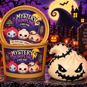 May include: A round cardboard container labeled Mystery Dumpling Cake Pop with illustrations of three characters, and a cream-colored dumpling-shaped cake pop with black stitched details and a menacing face sitting in front of the container.