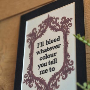 K&ouml;nnte beinhalten: Ein gerahmtes Kunstwerk mit dem Text "I'll bleed whatever colour you tell me to." Der Text ist schwarz, umgeben von einem burgunderfarbenen dekorativen Rahmen. Das Kunstwerk ist vor einem wei&szlig;en Hintergrund platziert und schwarz gerahmt.